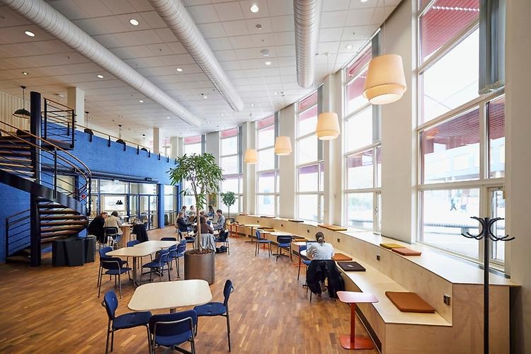 JMW-salen with big windows and lamps hanging from the roof. There are tables and chairs and one student is sitting by a table.
