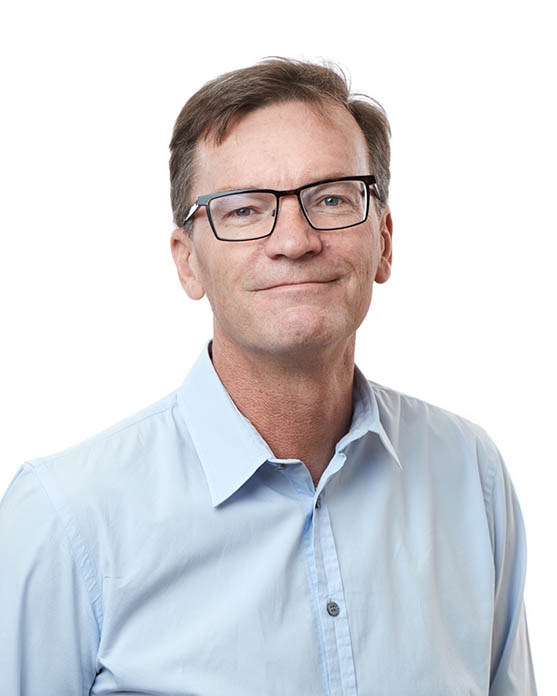 Man wearing glasses and a light blue collared shirt, facing forward and smiling slightly, posed against a white background.